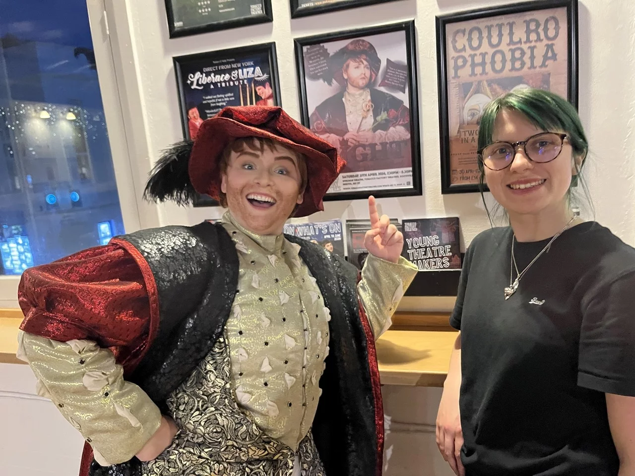 A selfie with Billie-Jo Rainbird standing on the right and Hannah Clift in drag as Henry the eighth on the left. Hannah is pointing at a poster of her show Eight.