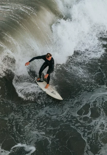 Surfista em uma onda grande, com a prancha, demonstrando surfe em mar agitado. Foto para web design.