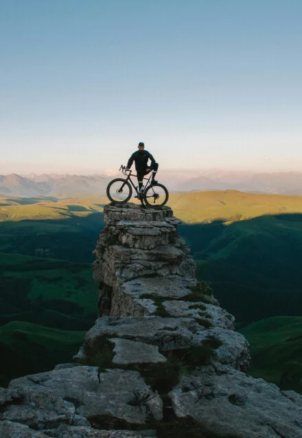 Homem com bicicleta de montanha no topo de uma rocha, em um ambiente natural. Web design de portfólio de esportes outdoor.