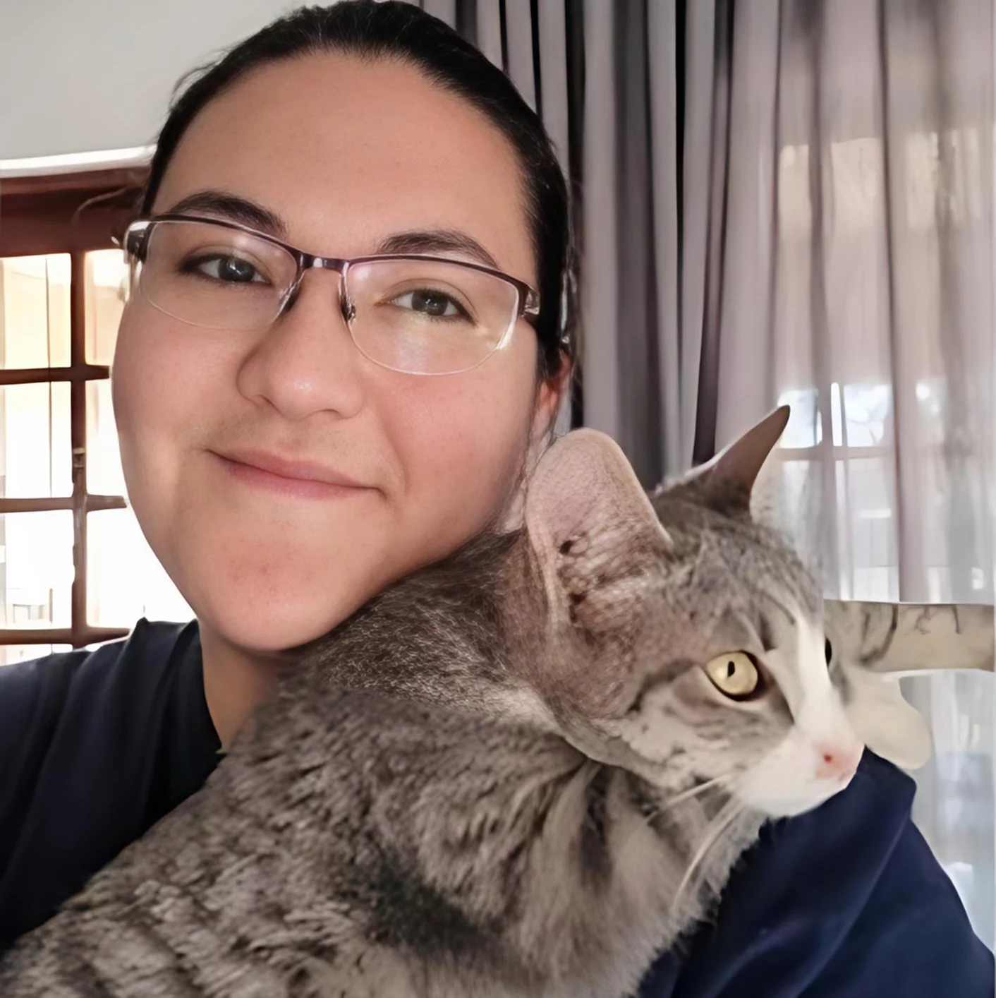 Adoption ten: Cat. A full grown tabby cat was adopted by a young woman with glasses. She is standing inside her house while taking the picture. The cat is resting peacefully on her shoulder and even thought the cat is awake you can see he is ready to dose off on his new owner's shoulder.