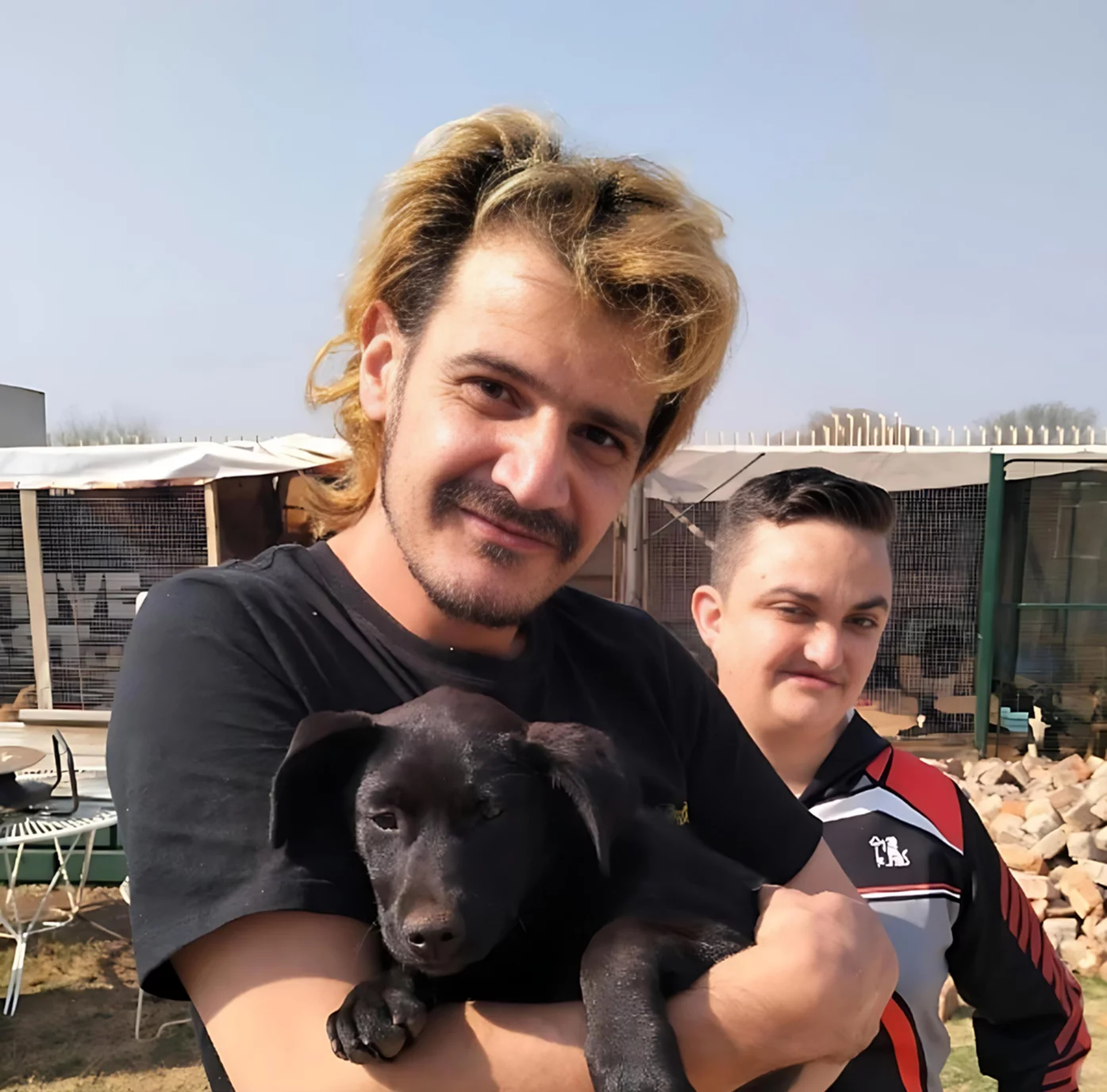 Adoption one: Dog. A cute little black puppy got adopted by two men. The man who is holding the puppy proudly has a moustache and blond hair. He is wearing a black T-shirt that makes seeing the puppy a little bit difficult ,however you can still see the puppy's adorable face!