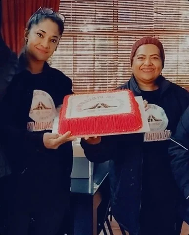 Image of the founder Shafeena Osman on the left and the most important director Tanya to the right. Both of them are holding a cake with the non profit's logo on it. The sides of the cake is red. Red is one of the company colours including teal and white. Both the founder and the director have Osman merchandise on.