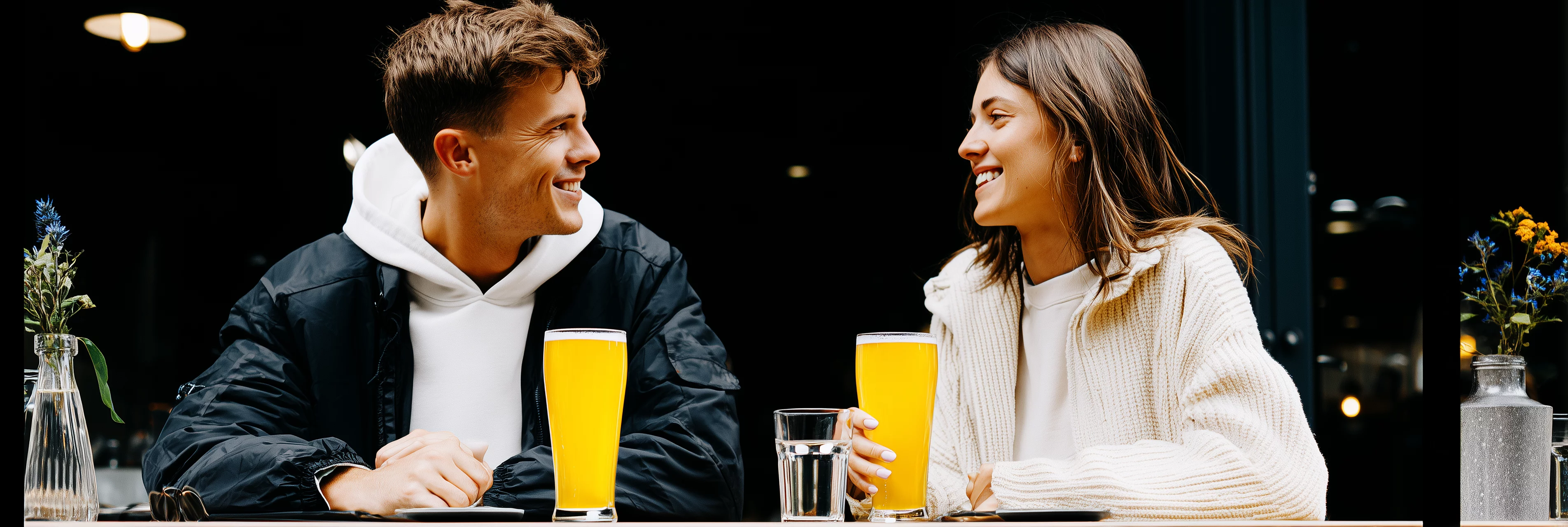 Casal sentado na mesa de um bar moderno, ambiente urbano, conversando e tomando um copo de chope