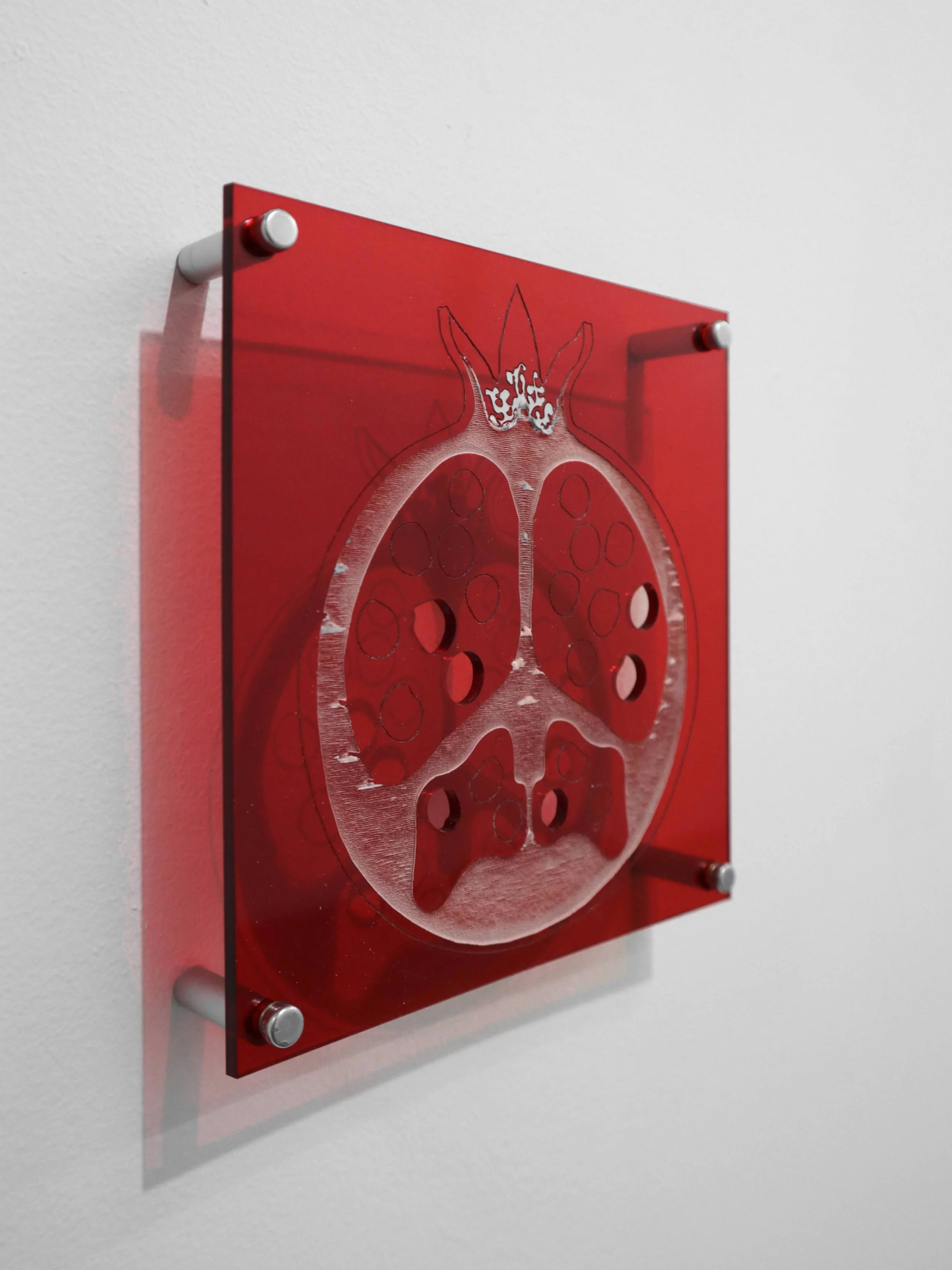 “Forbidden Fruit,” 2024, wall-mounted artwork by Grigorios Ilaridis at Base-Alpha Gallery, Antwerp. A red transparent rectangular plexiglass panel with a laser-etched sliced pomegranate design and six missing seeds represented by circular holes. The panel is mounted away from the wall with four matte silver rods, creating a floating effect and highlighting its translucent quality. Materials: Metal, red transparent plexiglass. Dimensions: 15 x 16 x 3.5 cm.