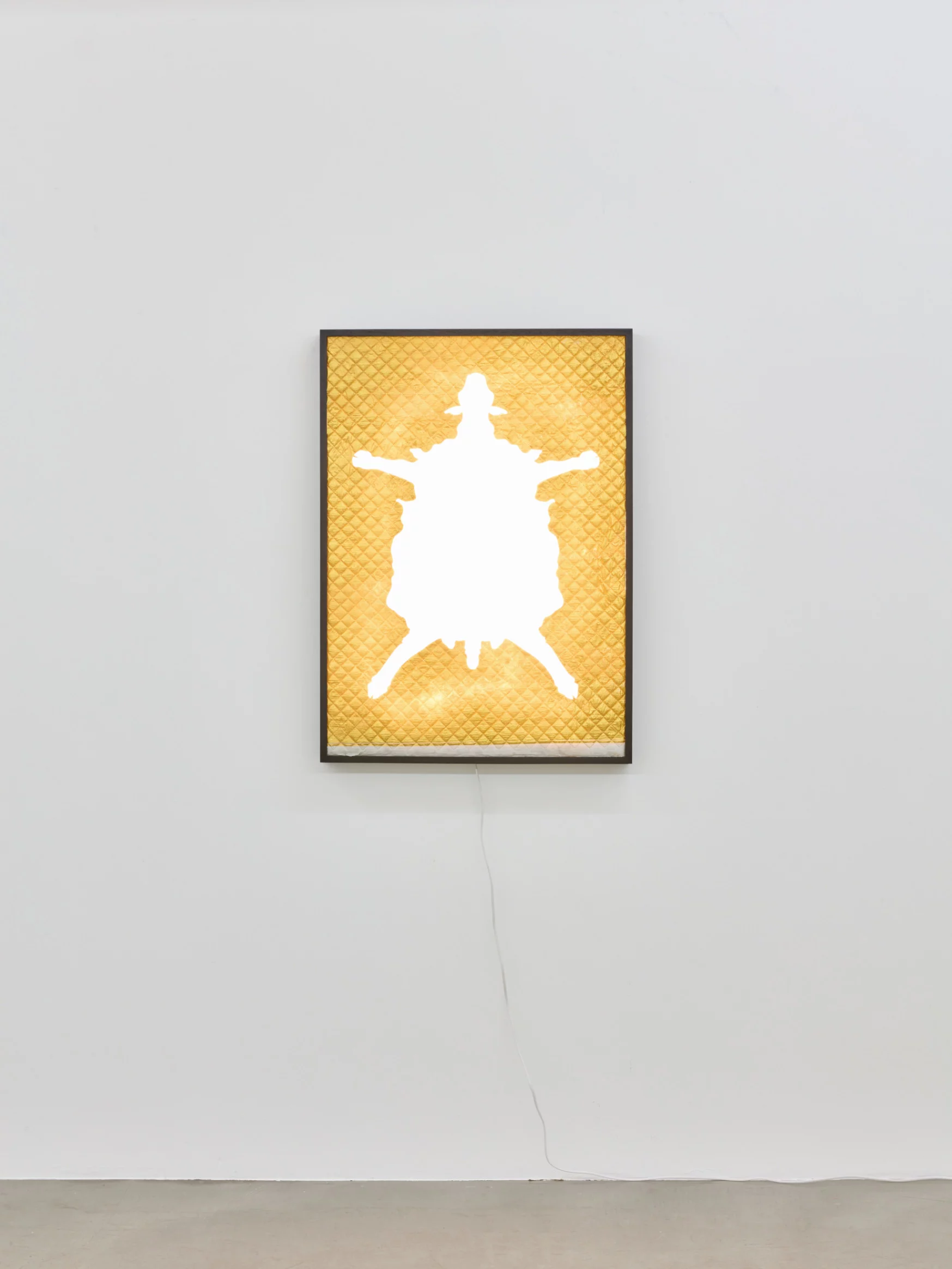 "Golden Fleece," 2024, lightbox-style sculpture by Grigorios Ilaridis at Base-Alpha Gallery, Antwerp. A diamond-quilted golden fleece cutout rests on an opaque white plexiglass background, backlit by warm LED lighting that enhances texture and creates a relic-like aura. Framed in black wood, the artwork blends mythological significance with contemporary design. Dimensions: 68 x 95 x 7 cm.