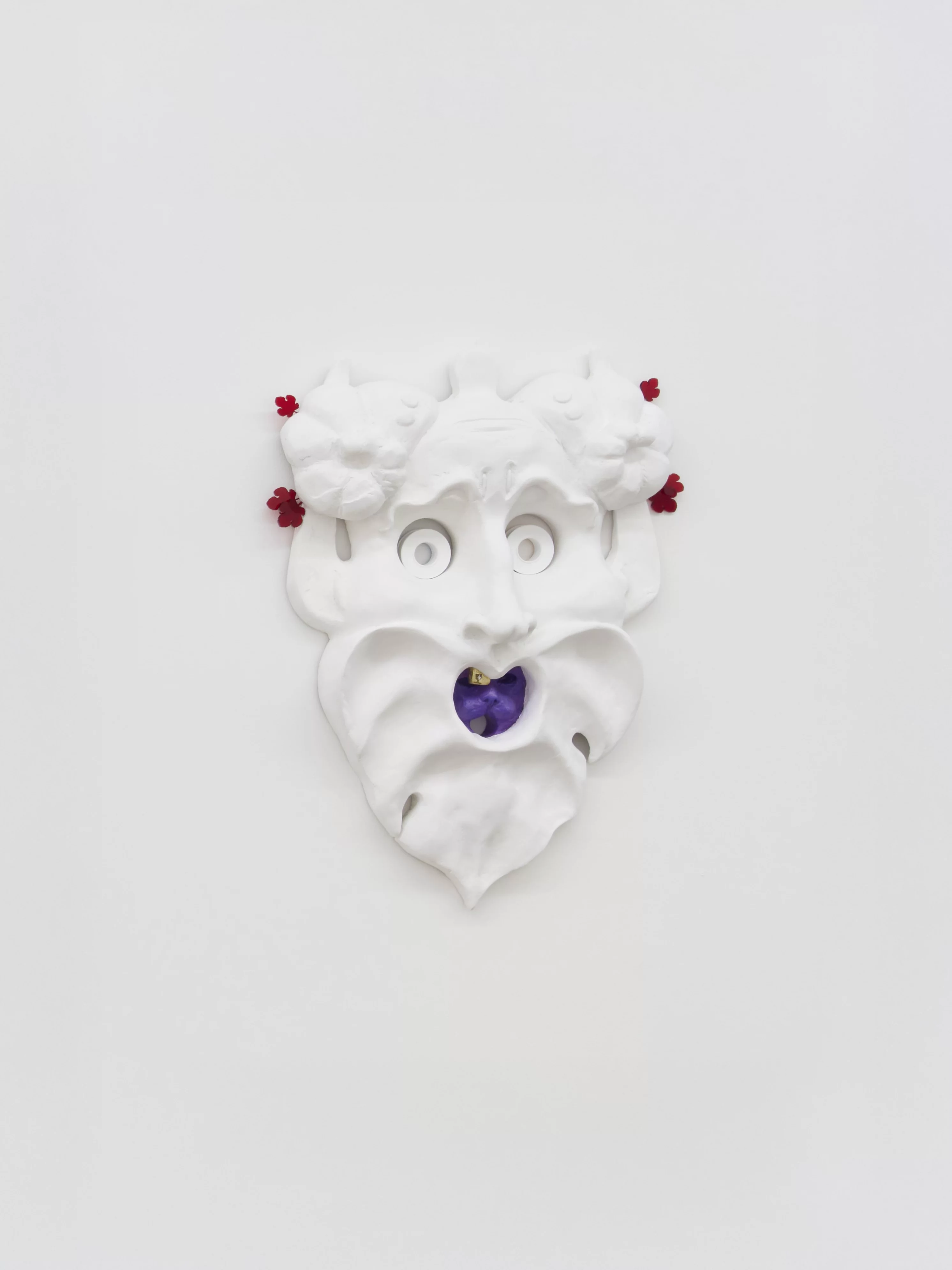Oral Tradition III" a satyr-inspired sculpture by Grigorios Ilaridis at Base-Alpha Gallery in Antwerp. The mask is painted white, with serpent-like eyebrows, upward-looking eyes, and a head bump. It has a single golden tooth decorated with a brass chalice and acrylic diamond, while a purple cat face appears inside the open mouth. Made from acrylic, resin, and brass. Dimensions: 62 x 47 x 12 cm.