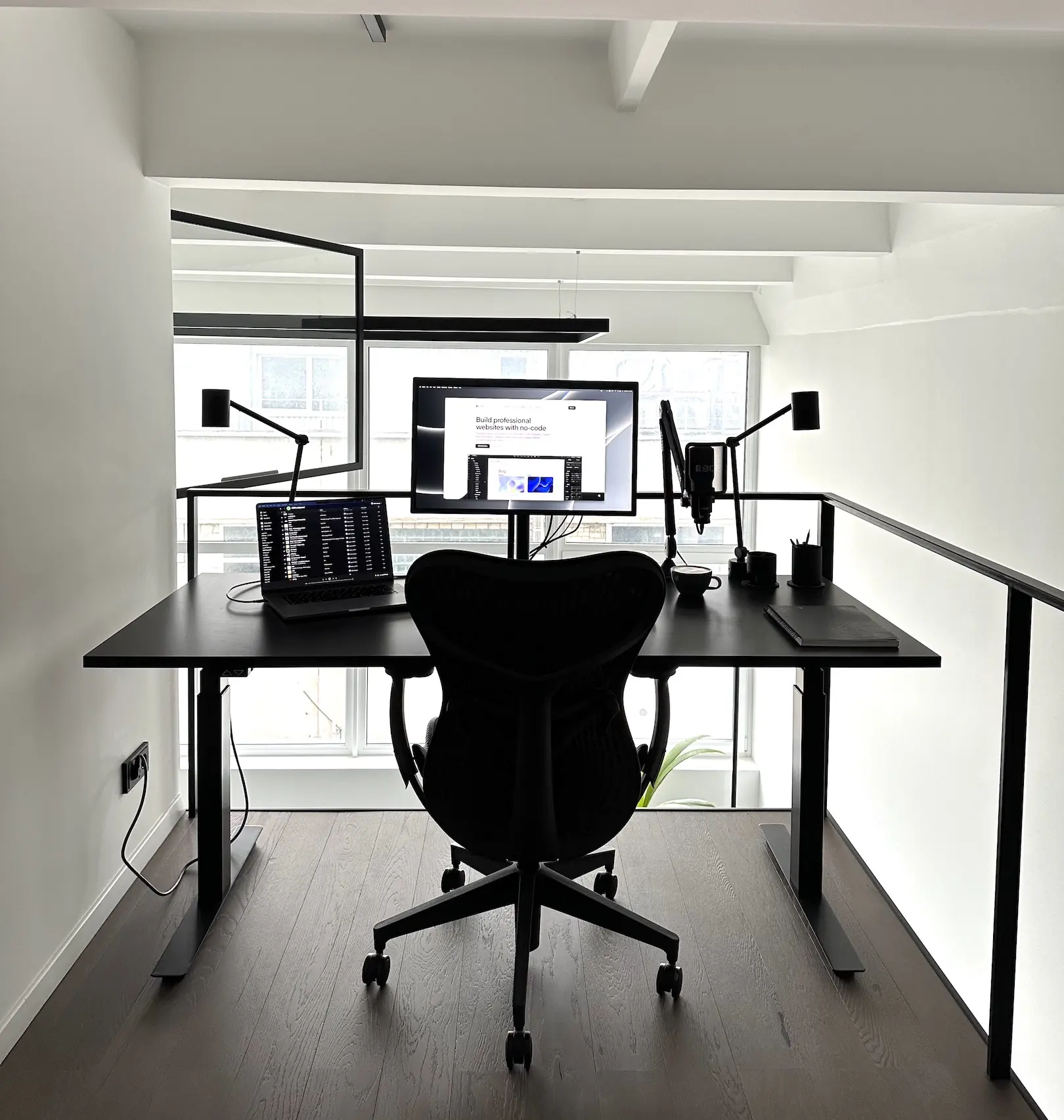 minimal WFH setup for a visual designer including MacBook Pro, microphone, cup of water, notebook, pencils and pens, and an external screen