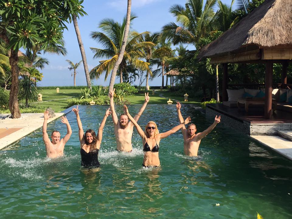 Five The Remote Company employees are waving from the swimming pool in Bali.